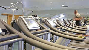 A row of stationary exercise bikes with digital displays, a ceiling with recessed lighting, and a wooden door in the background.