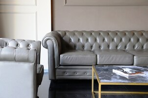 A grey leather sofa with a tufted backrest and armrests, a matching armchair, and a marble coffee table with a magazine.