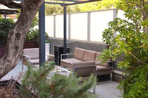 An outdoor patio area with a beige sofa, a small table, and a tall planter.