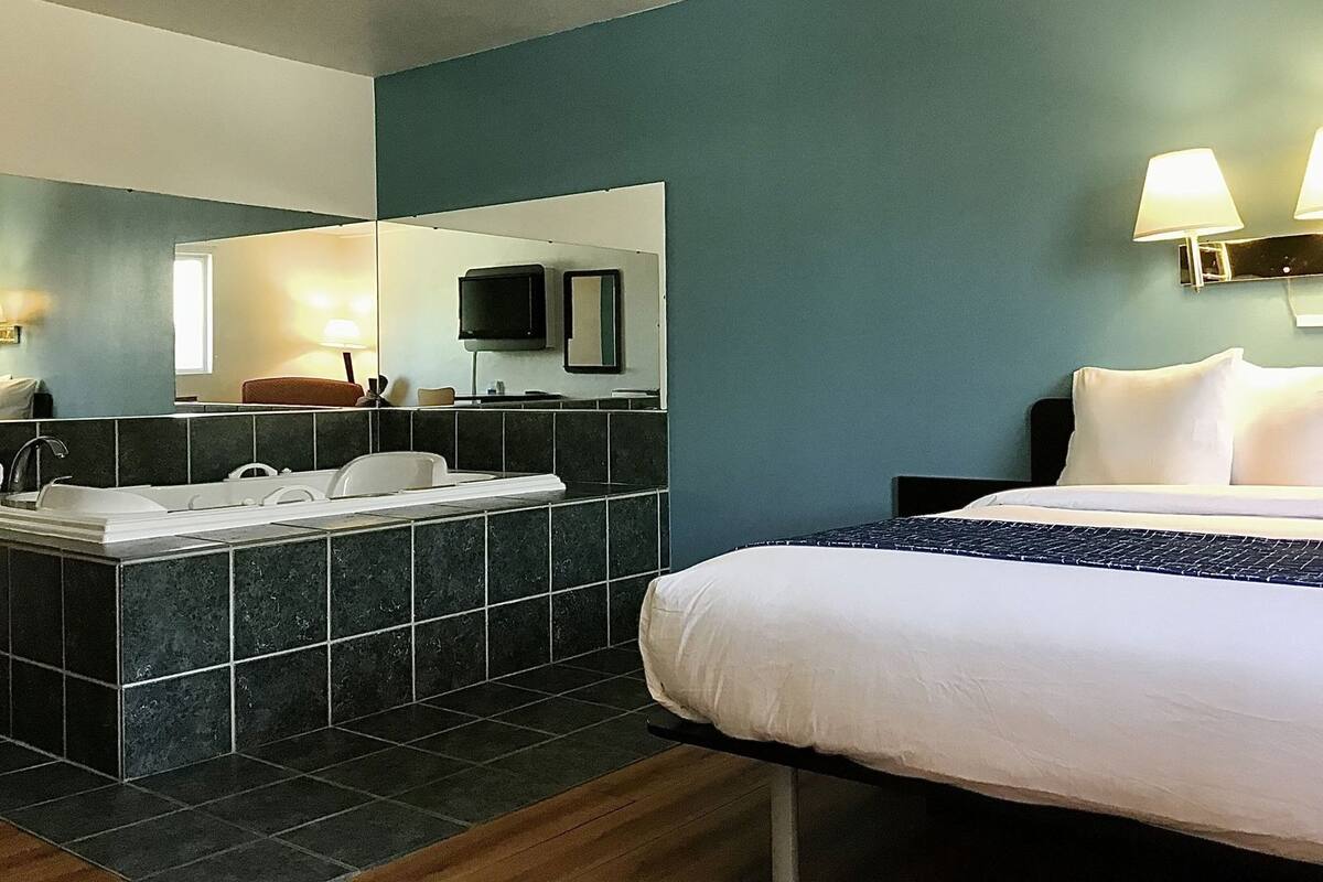 A hotel room with a bed, a bathroom with a bathtub, a mirror, and a television.