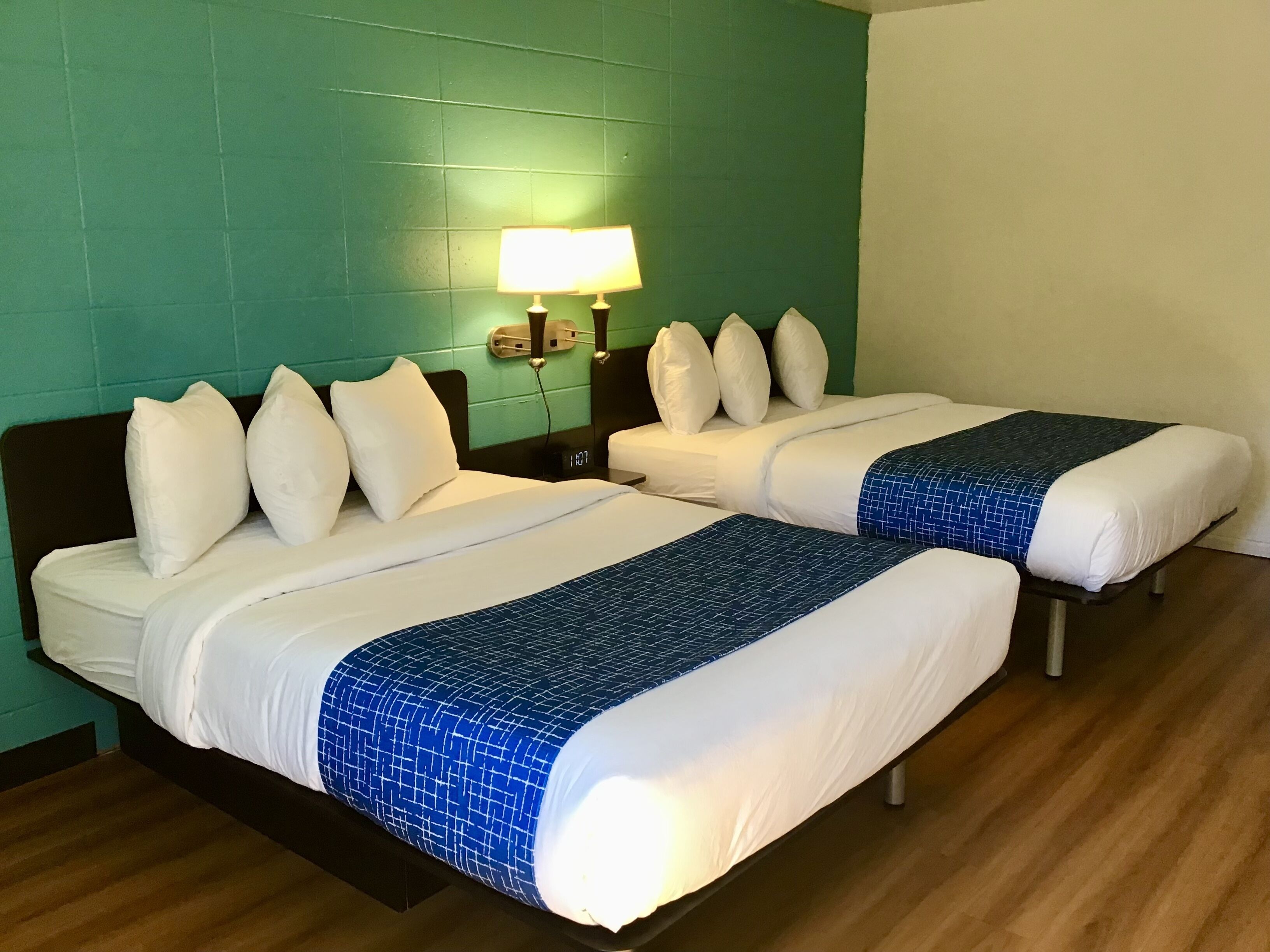 Deux lits jumeaux avec du linge de lit blanc et des couvre-lits à motifs bleus, dans une chambre d’hôtel aux murs de couleur turquoise et au plancher en bois.