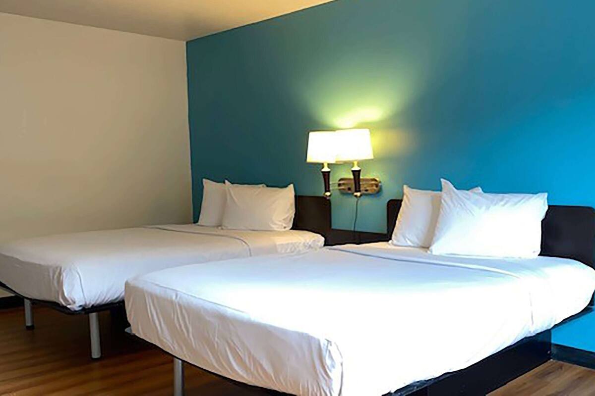 A hotel room with two single beds and a larger bed. There is a nightstand with a lamp between the beds.