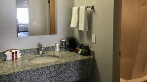 A bathroom with a granite countertop sink, a mirror, a towel rack with two towels, a coffee maker, and toiletries. - Travelodge Inn & Suites by Wyndham Missoula University Park (Missoula)