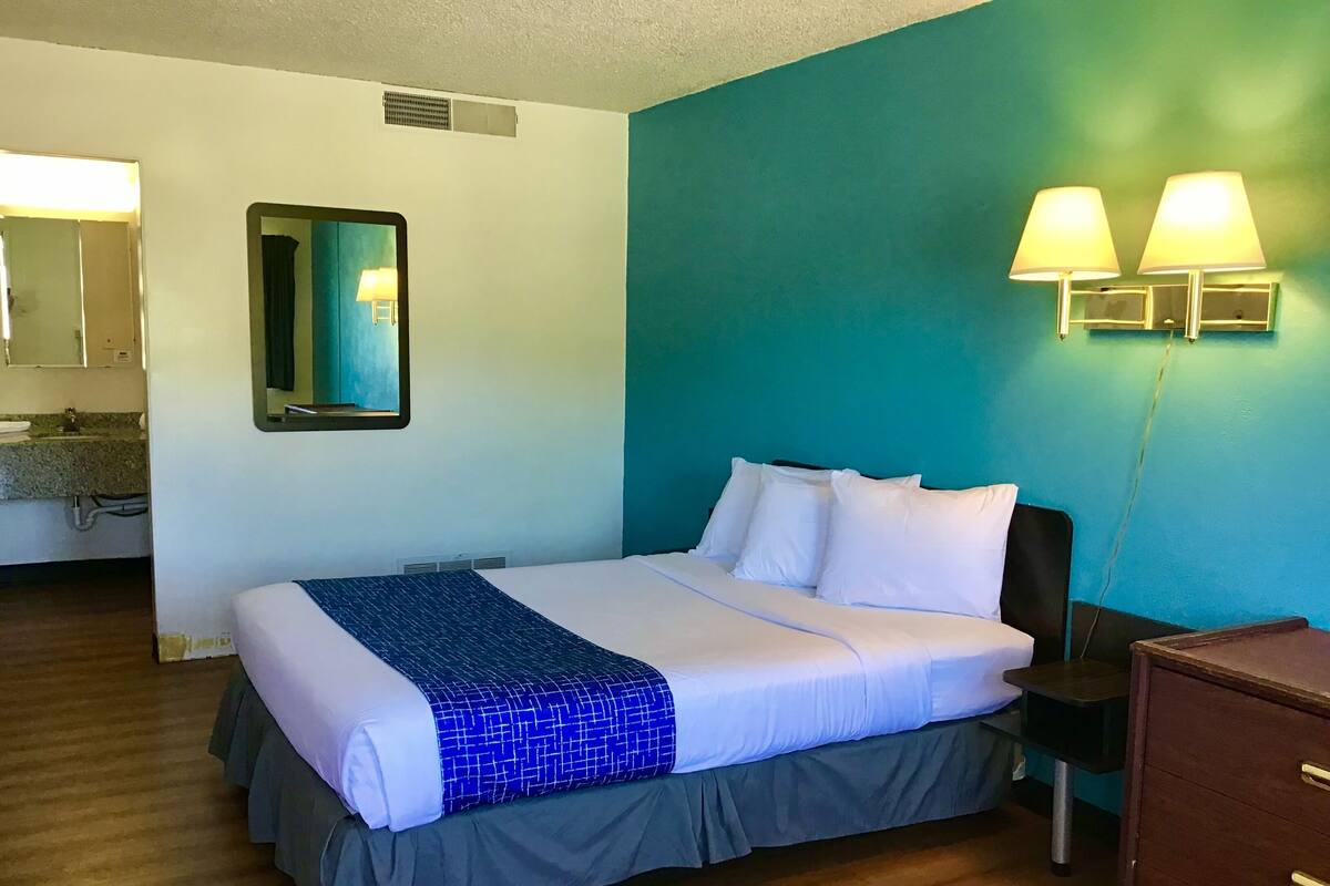 A hotel room with a bed, a nightstand, a dresser, a bathroom with a sink, and a mirror.