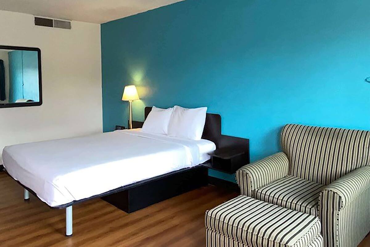 A hotel room with a bed, a nightstand, a lamp, and a striped armchair.