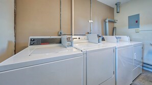 Un espace buanderie équipé d’un lave-linge et d’un sèche-linge à chargement frontal, d’un panneau de commande et d’une bouche d’aération fixée au mur.