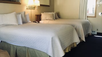 Een hotelkamer met twee bedden, een nachtkastje, een lamp, een spiegel en een raam met gordijnen.