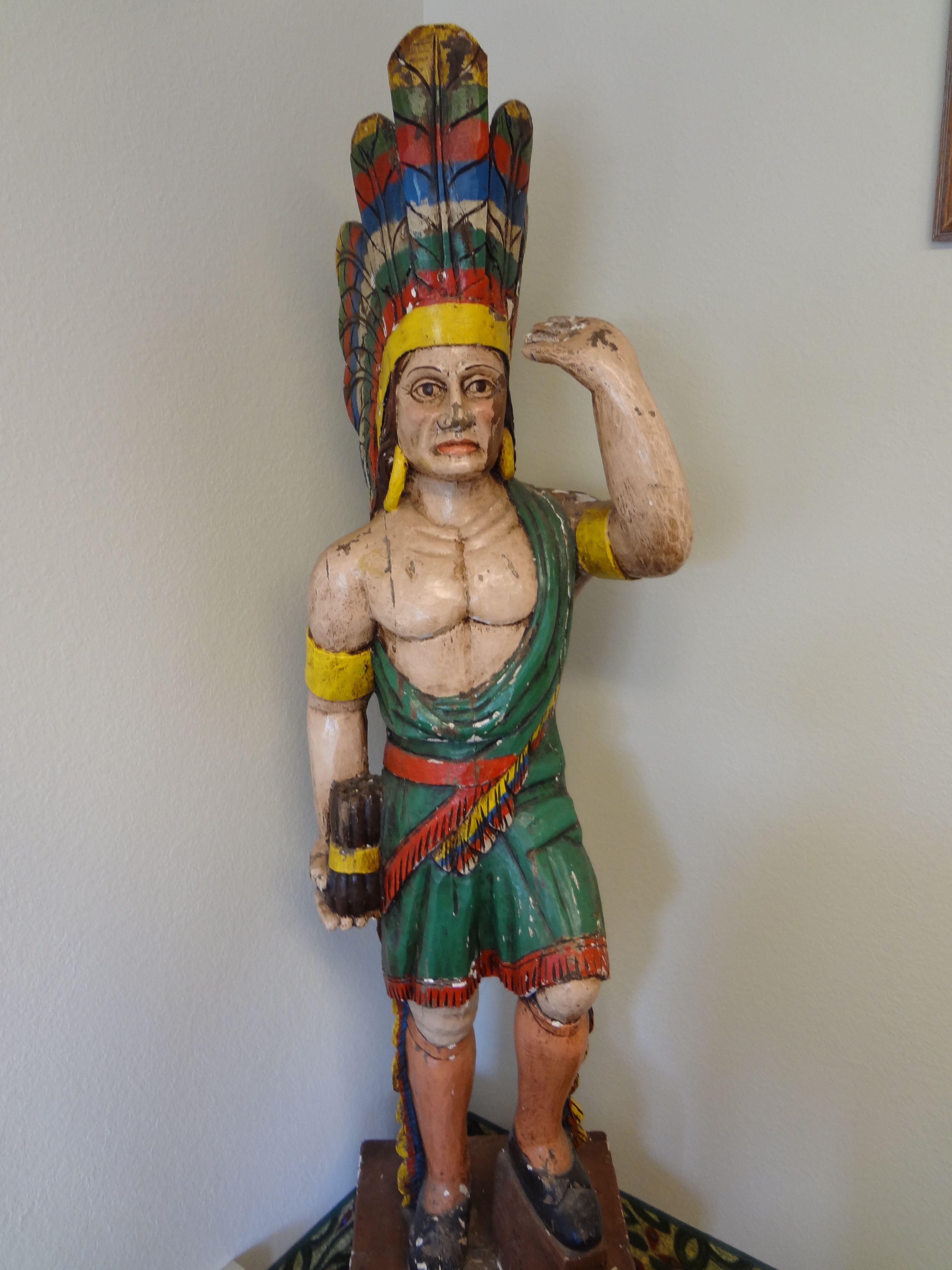 A wooden statue of a figure with a headdress, green and red attire, and a raised hand.