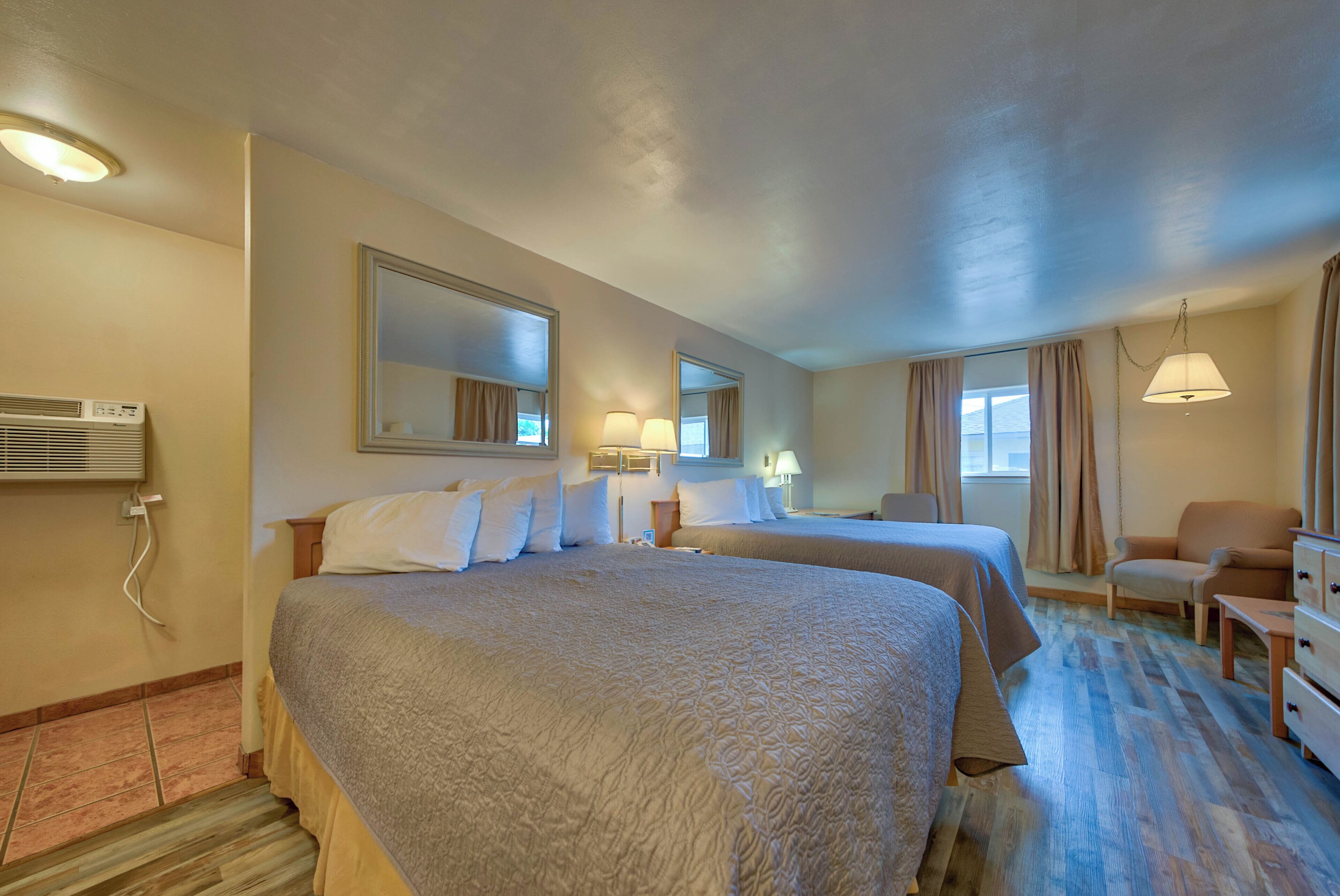 Habitación de hotel con dos camas, una silla, un escritorio y una lámpara.