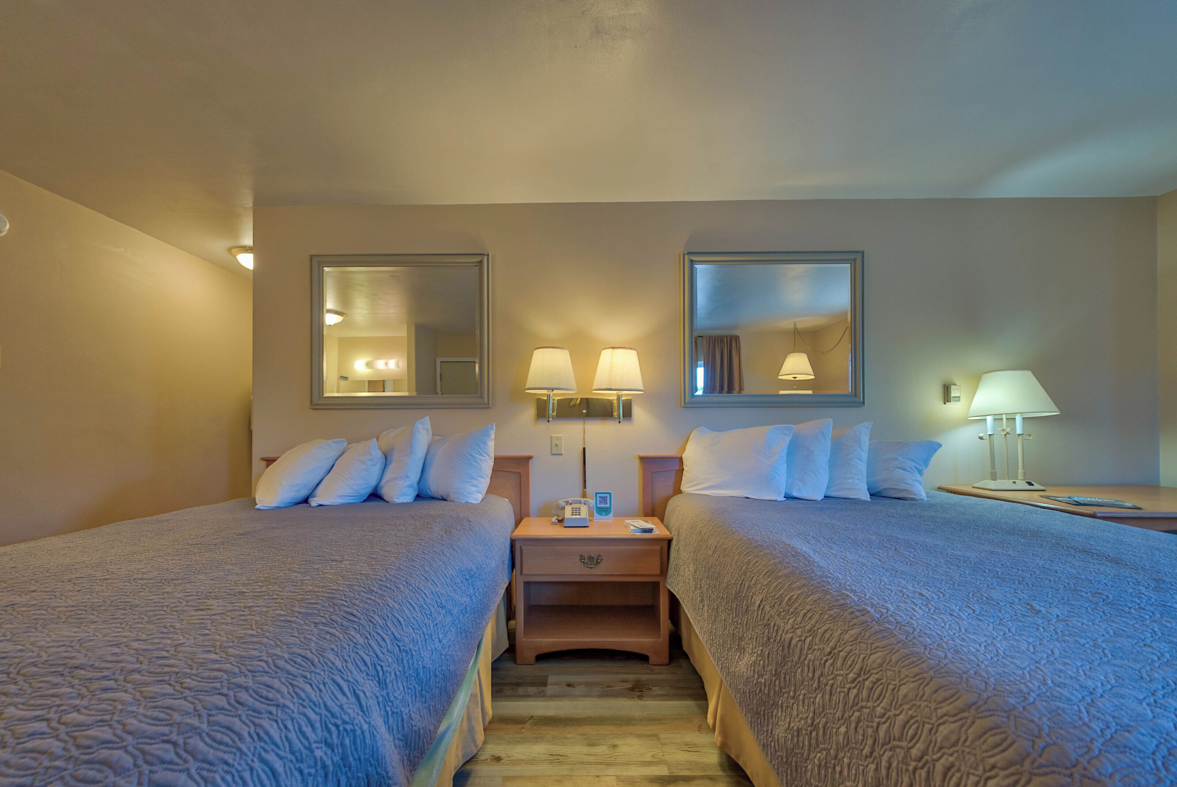 A hotel room with two beds, bedside lamps, a nightstand with a phone, and a mirror on the wall.