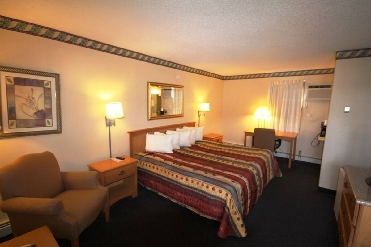 A hotel room with a bed, a chair, a desk, and a lamp.