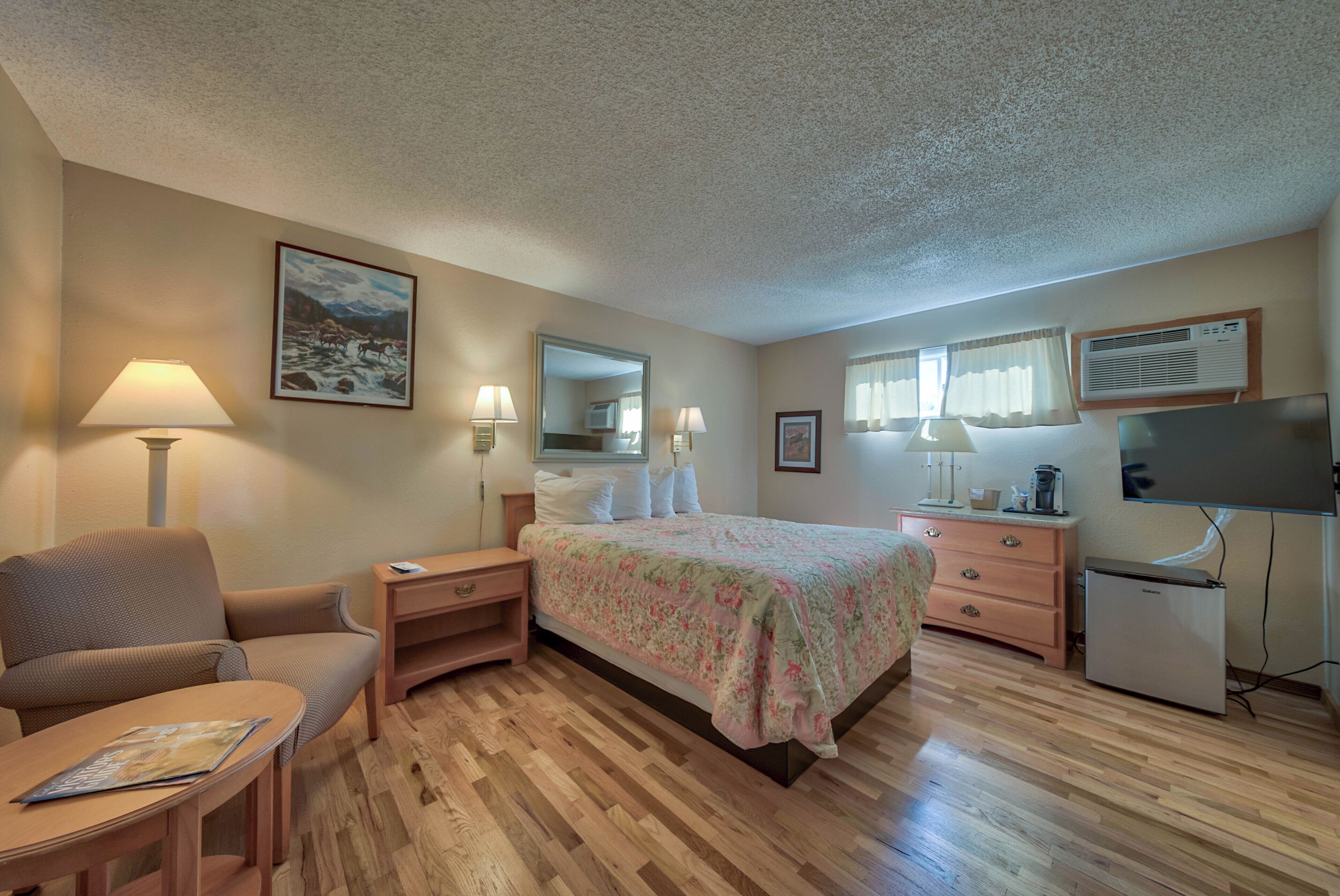A hotel room with a bed, a desk, a chair, a TV, and a refrigerator.