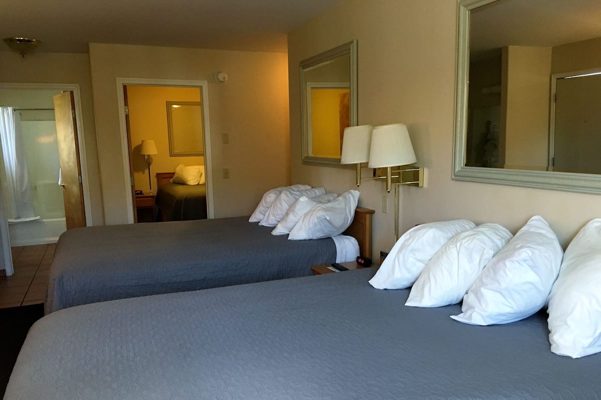 A hotel room with two beds, a bathroom, and a mirror.