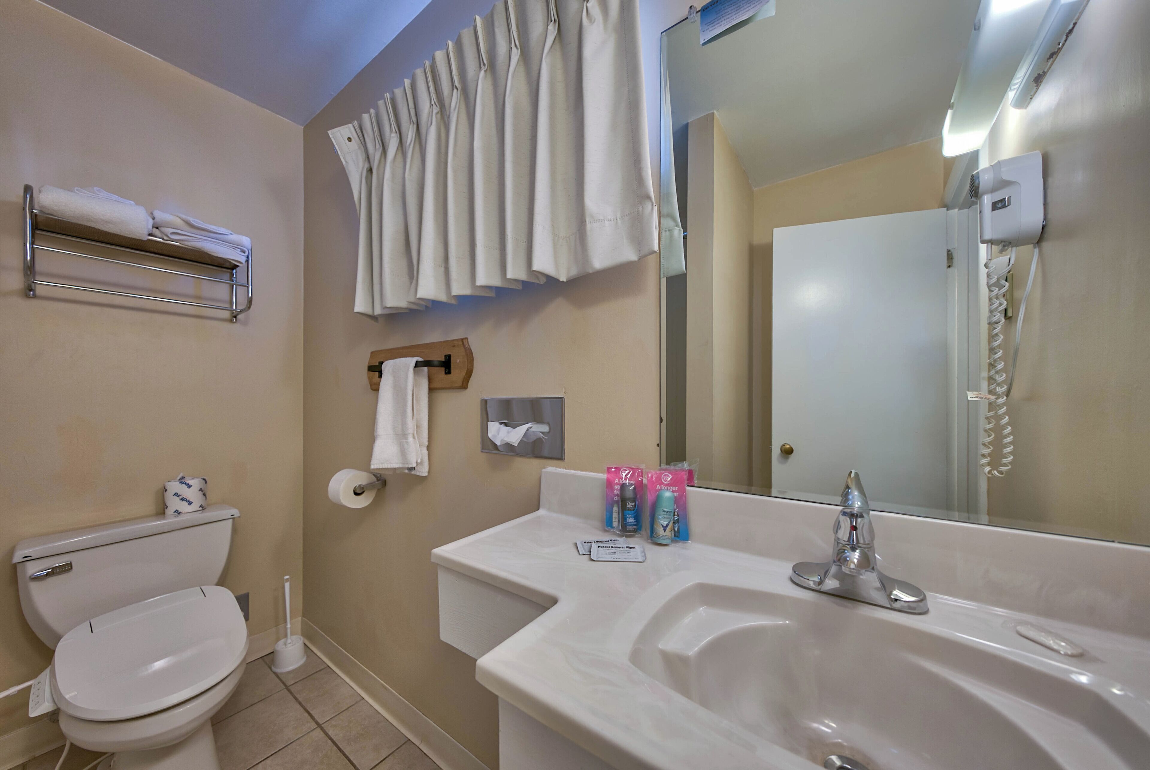 Ein Badezimmer mit Toilette, Waschbecken, Spiegel, Handtuchhalter und einer Duschvorhang.