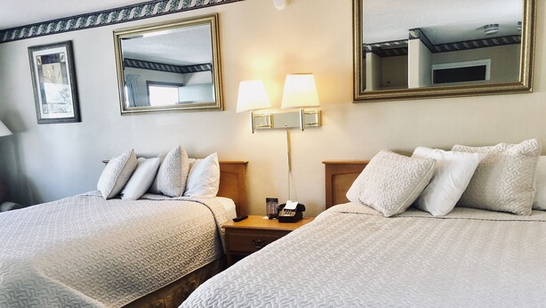 Une chambre d’hôtel avec deux lits, une table de chevet avec une lampe, un téléphone et deux miroirs fixés au mur.