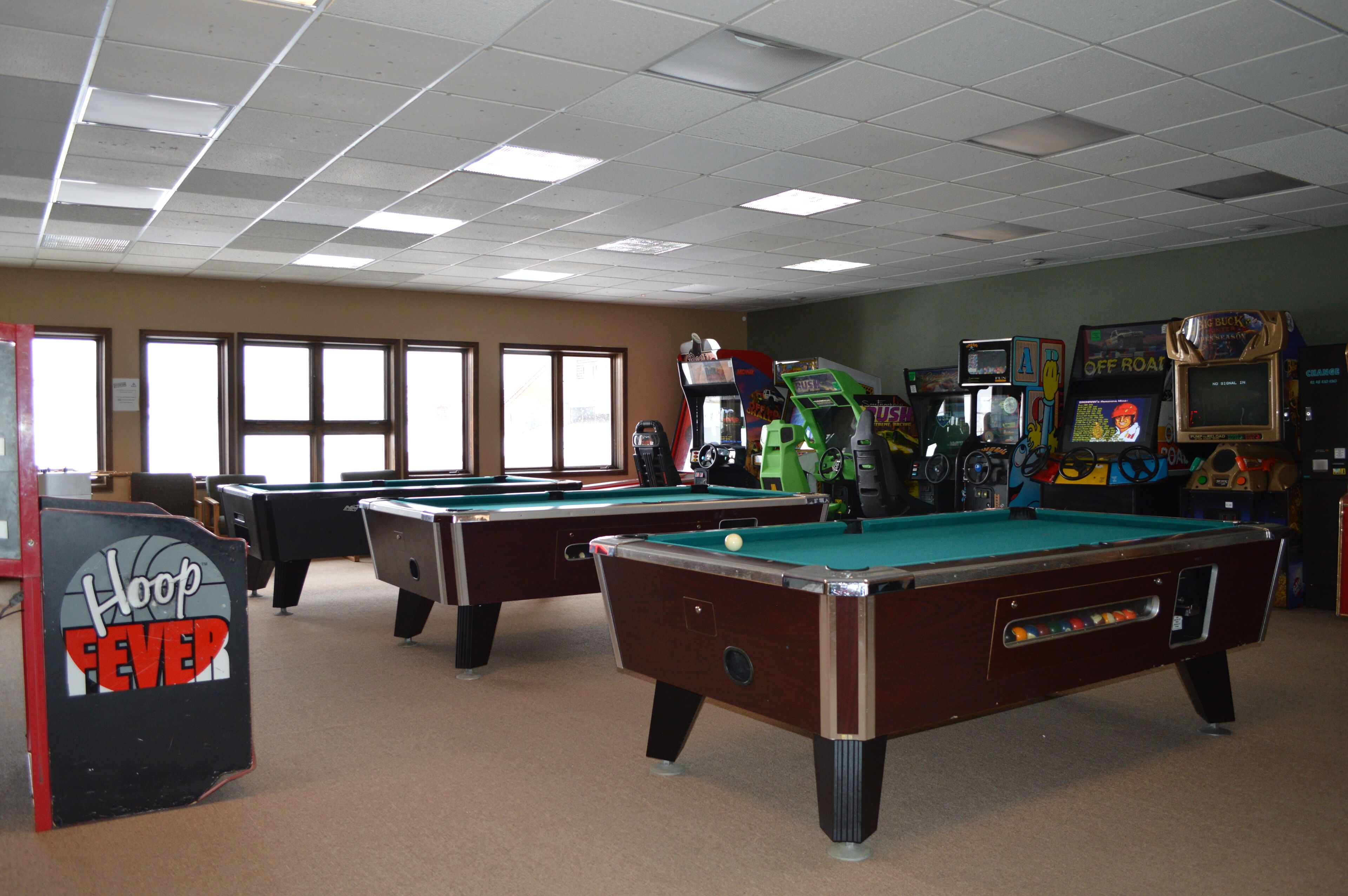 A pool hall with multiple pool tables, arcade games, and a sign that reads "Hoop Fever".