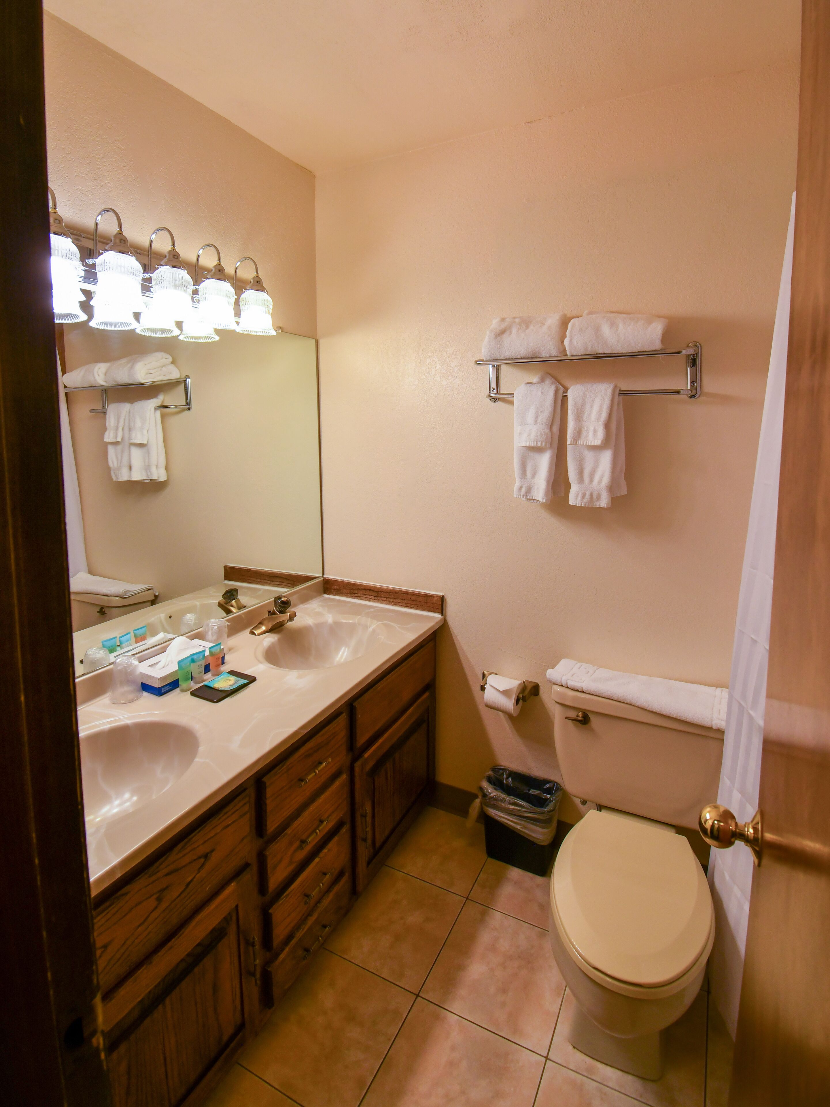 A bathroom with a sink, mirror, towel rack, toilet, and a trash bin.