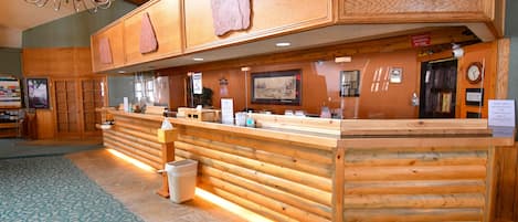 Un espace d’accueil avec un comptoir en bois, un lustre et un panneau indiquant que le port du masque est obligatoire.