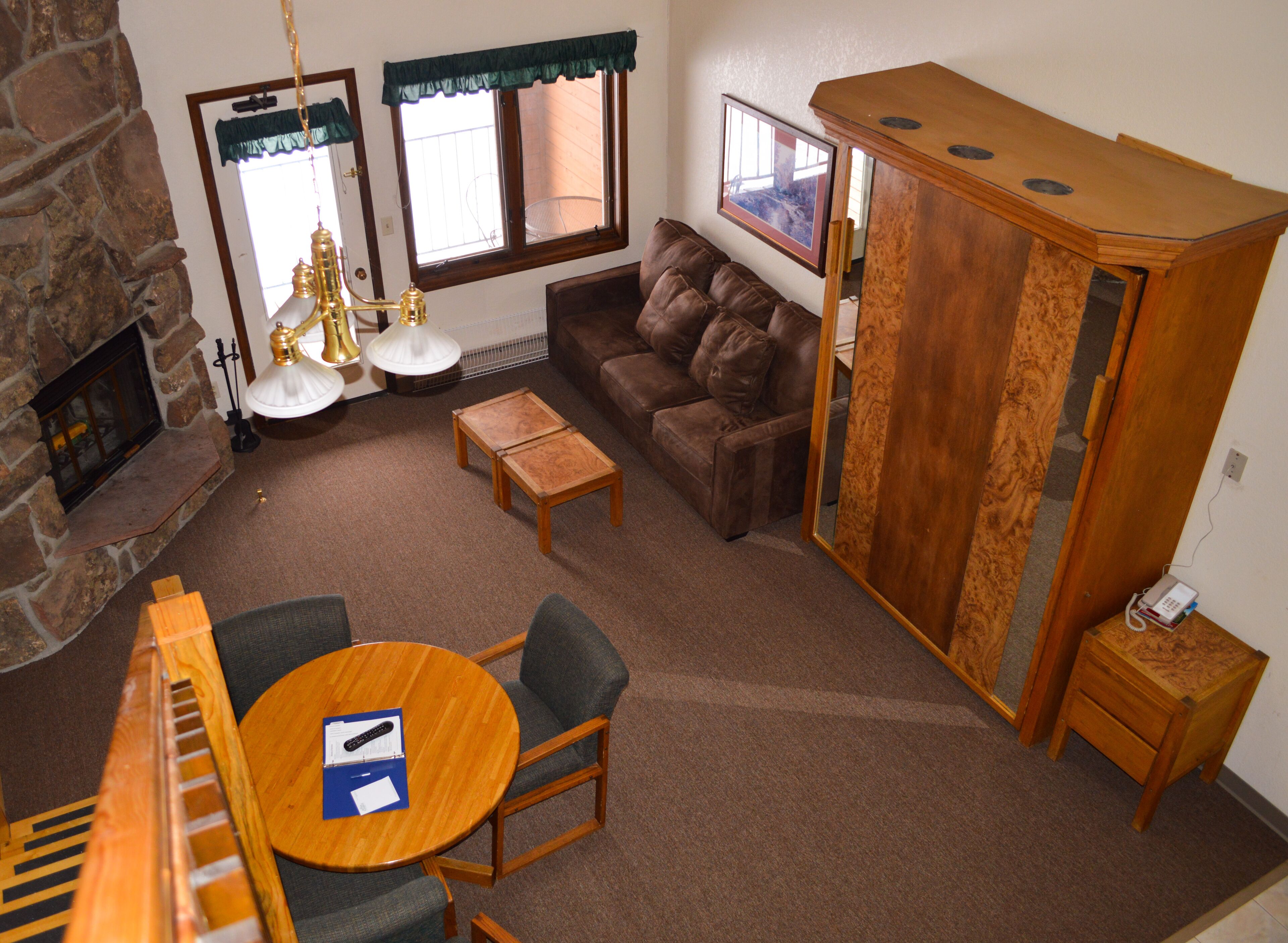 A cozy living room with a stone fireplace, a brown leather sofa, a wooden coffee table, and a small wooden cabinet.