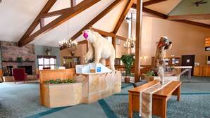 A spacious lobby with high ceilings and exposed wooden beams, featuring a stone fireplace, plush seating, and a polar bear statue.