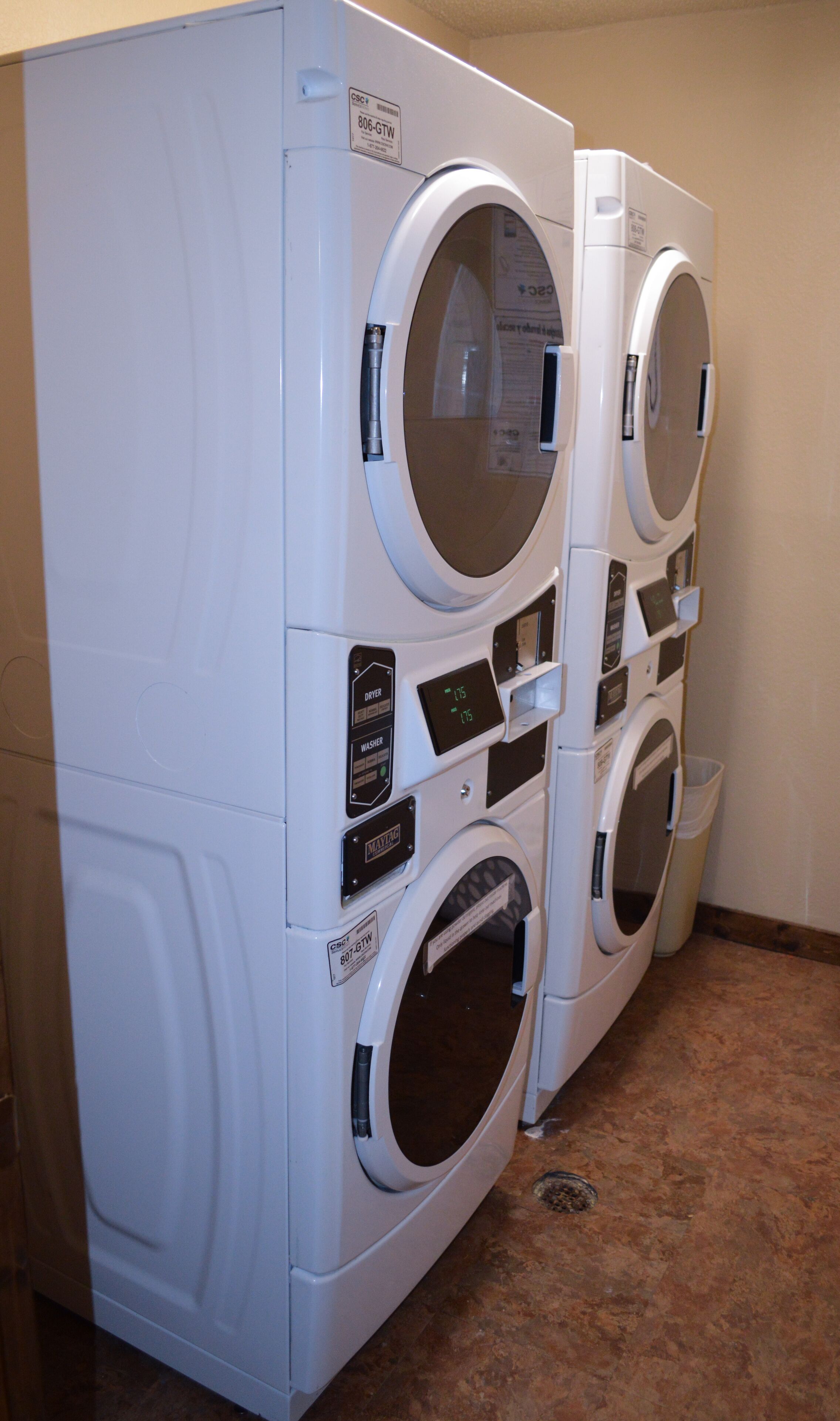 A row of white front-loading washers with control panels and a small trash bin.