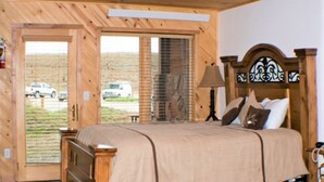 A wooden room with a bed, a door leading outside, and a window with a view of parked cars.