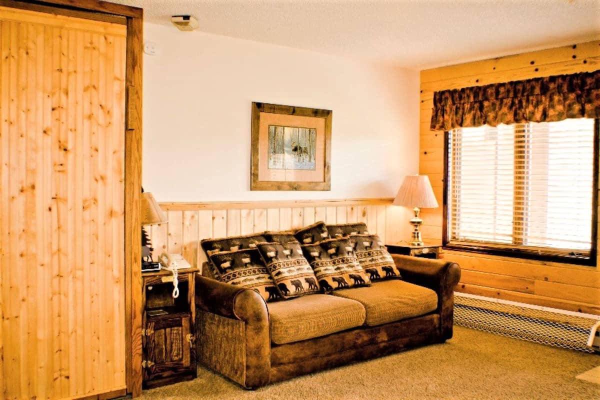 A cozy room with a wooden wall, a framed picture, a lamp, and a window with blinds.