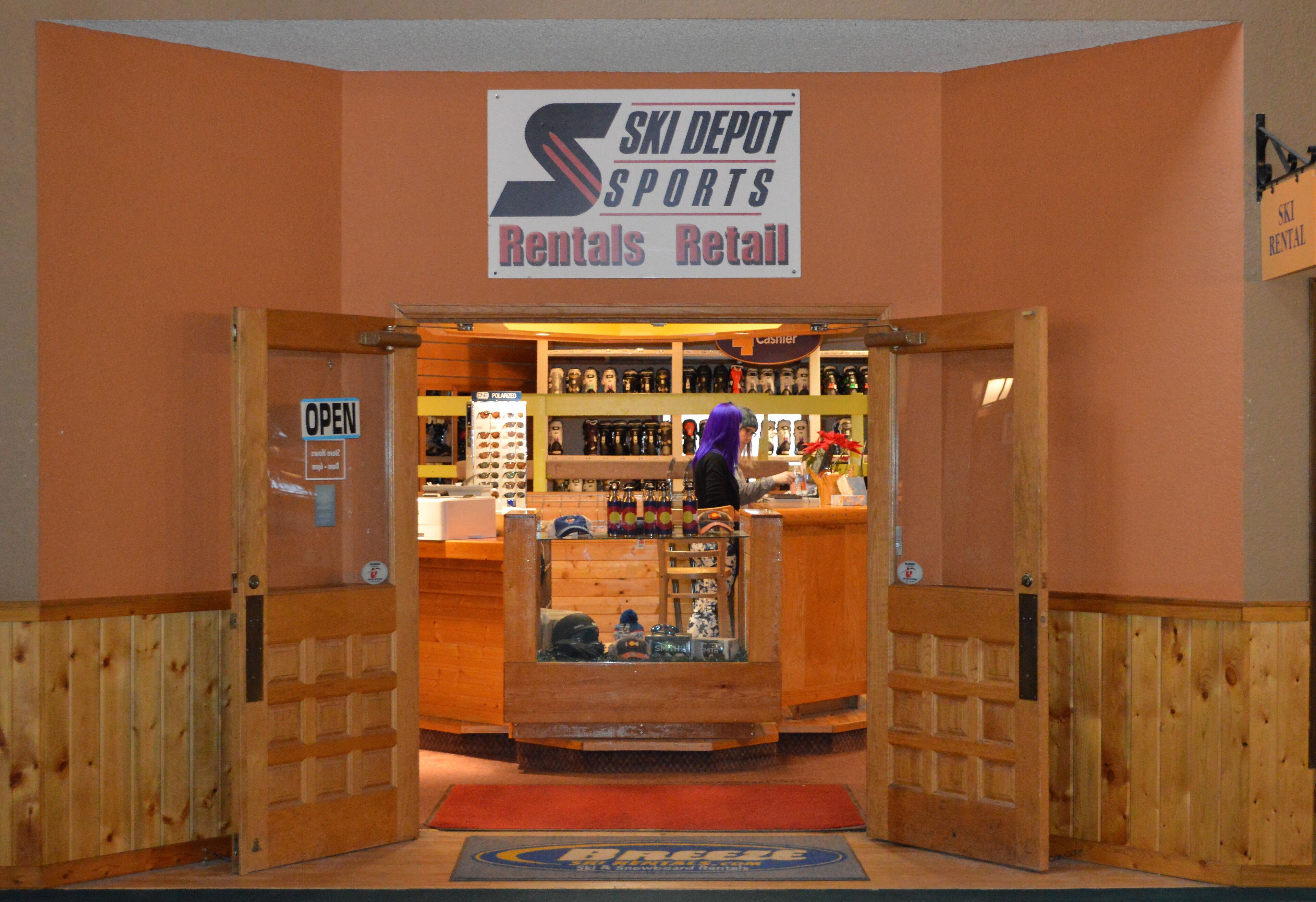 Un magasin de location de matériel de ski avec une enseigne indiquant : « Ski Depot – Location et vente d’articles de sport. »