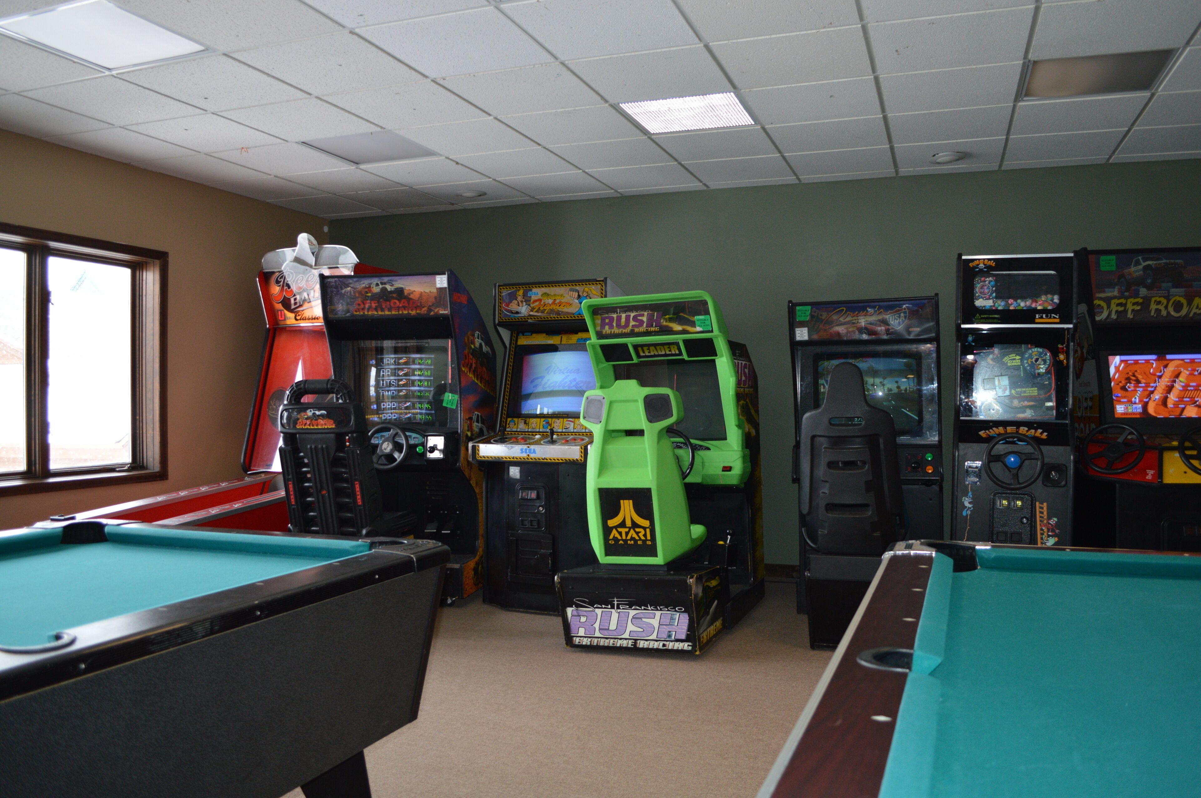 Habitación con mesas de billar y juegos de arcade, incluyendo 'Rush' y 'Off Road'.