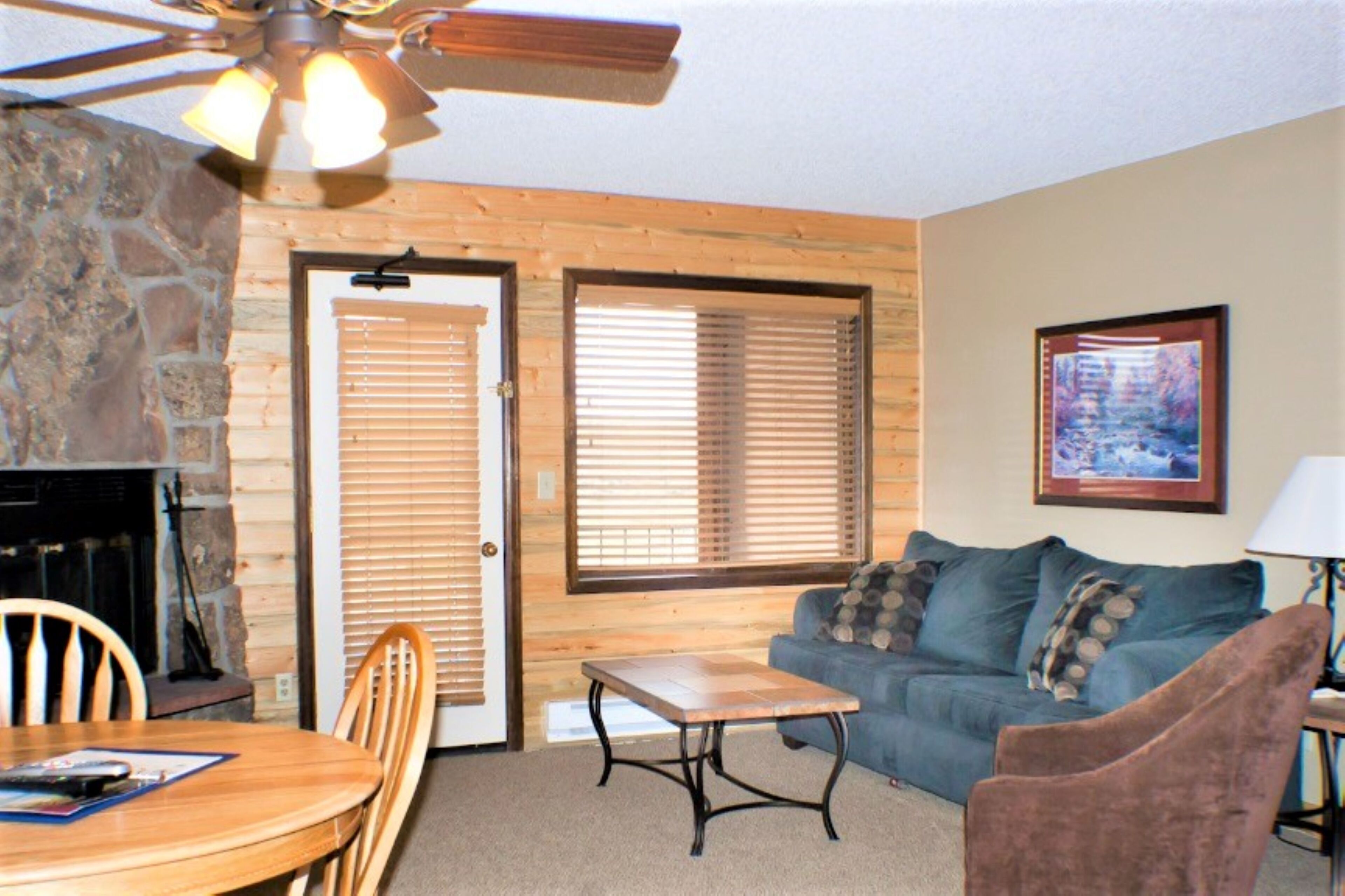 A cozy living room with a stone fireplace, wooden door, and a blue couch.
