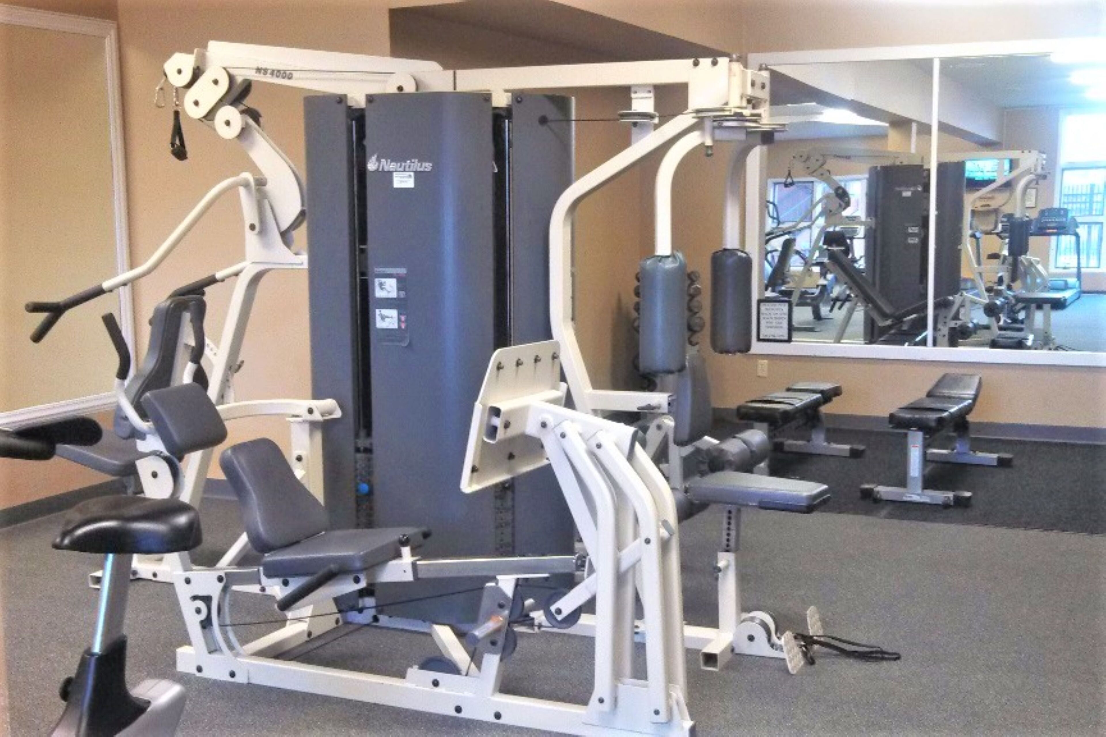 Un gimnasio con máquinas Nautilus, bancos y un espejo.