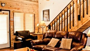 A wooden interior with a leather sofa, a chair, a lamp, and a staircase.