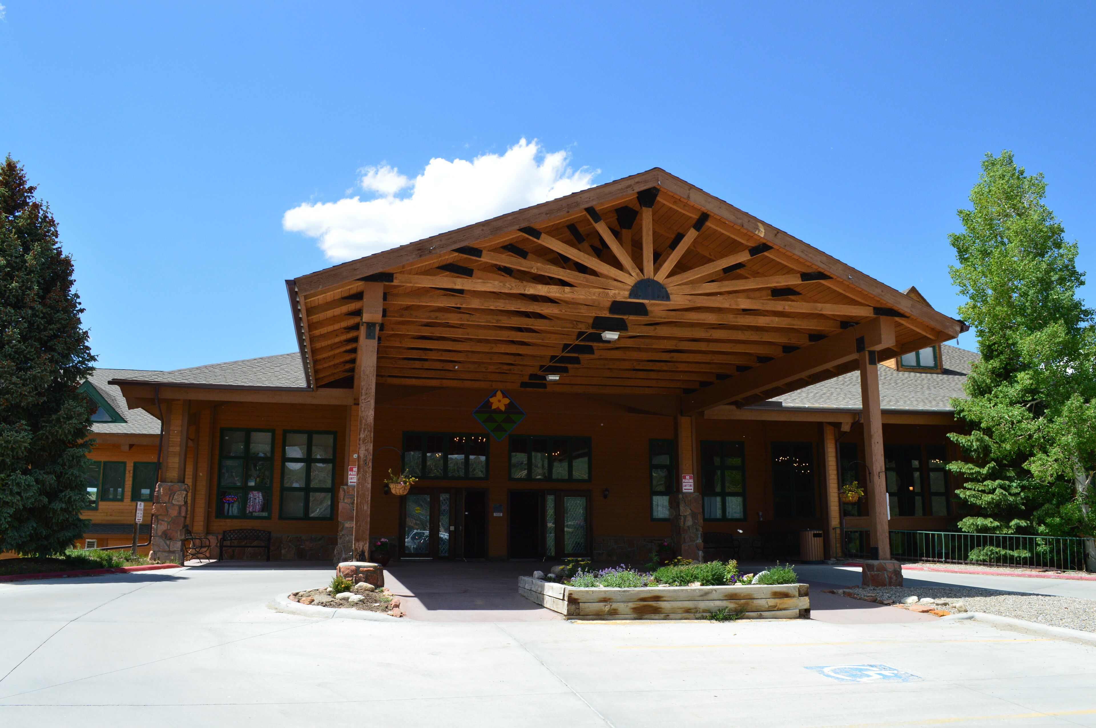 A building with a covered entrance, large windows, and a landscaped area with plants and a bench.