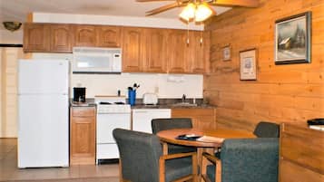 A kitchen with wooden cabinets, a refrigerator, stove, microwave, and a dining table with chairs.