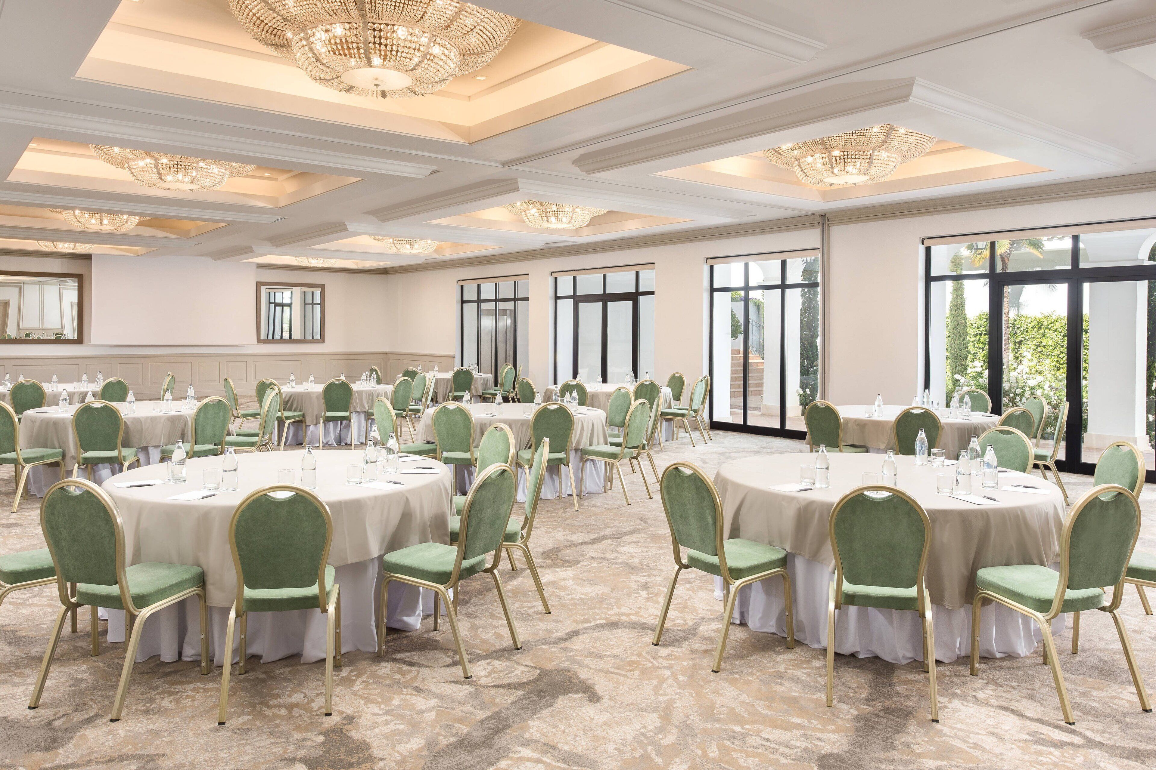 Un salón de banquetes con mesas redondas, sillas tapizadas en verde y candelabros.