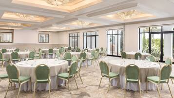 Un salón de banquetes con mesas redondas, sillas tapizadas en verde y candelabros.