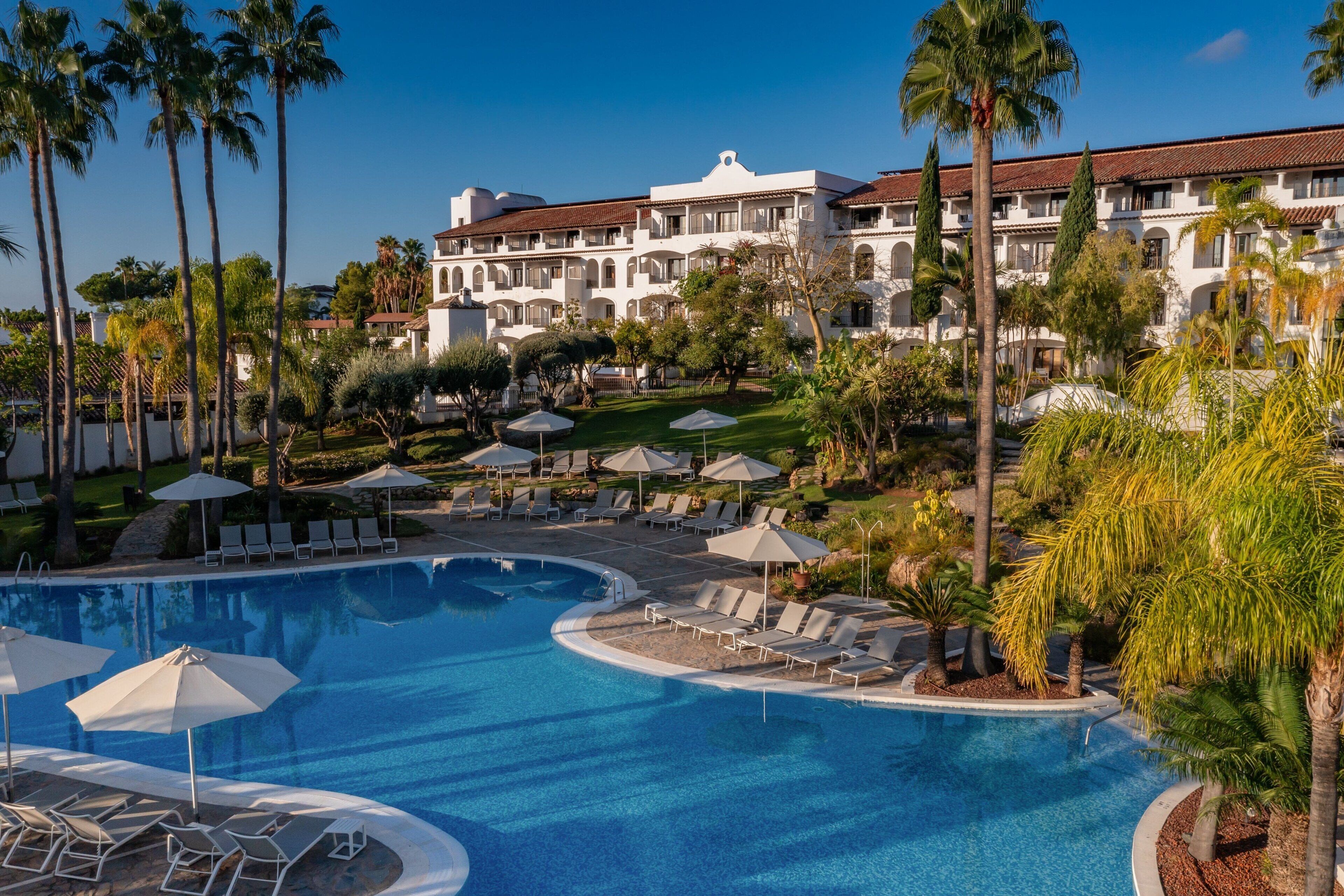 A resort with a large pool, sun loungers, umbrellas, and palm trees.