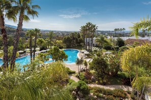 Una piscina rodeada de palmeras y vegetación, con vistas a un paisaje urbano al fondo.