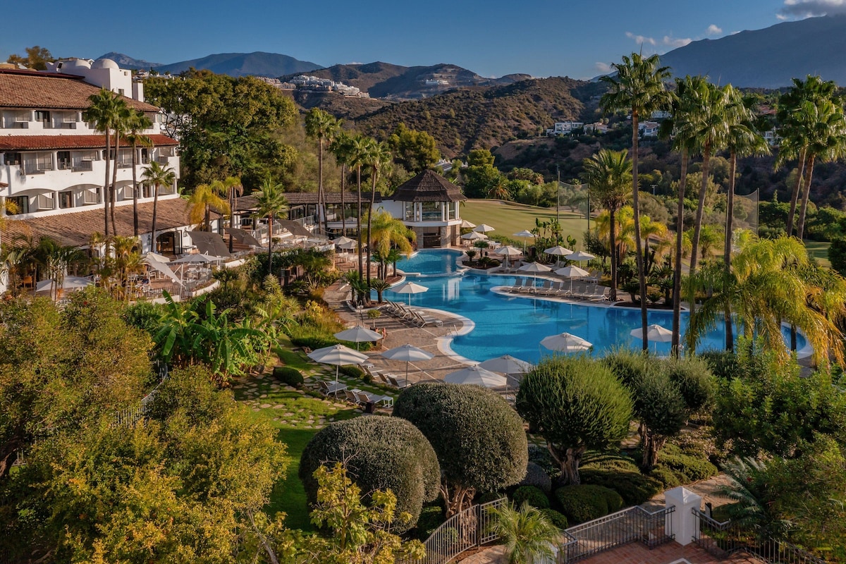 Un complexe hôtelier doté d’une grande piscine, de palmiers et offrant une vue sur un paysage montagneux.