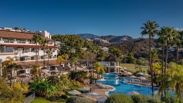 Relax by the resort's large pool surrounded by lush gardens and palm trees, with a scenic view of the surrounding hills and mountains.