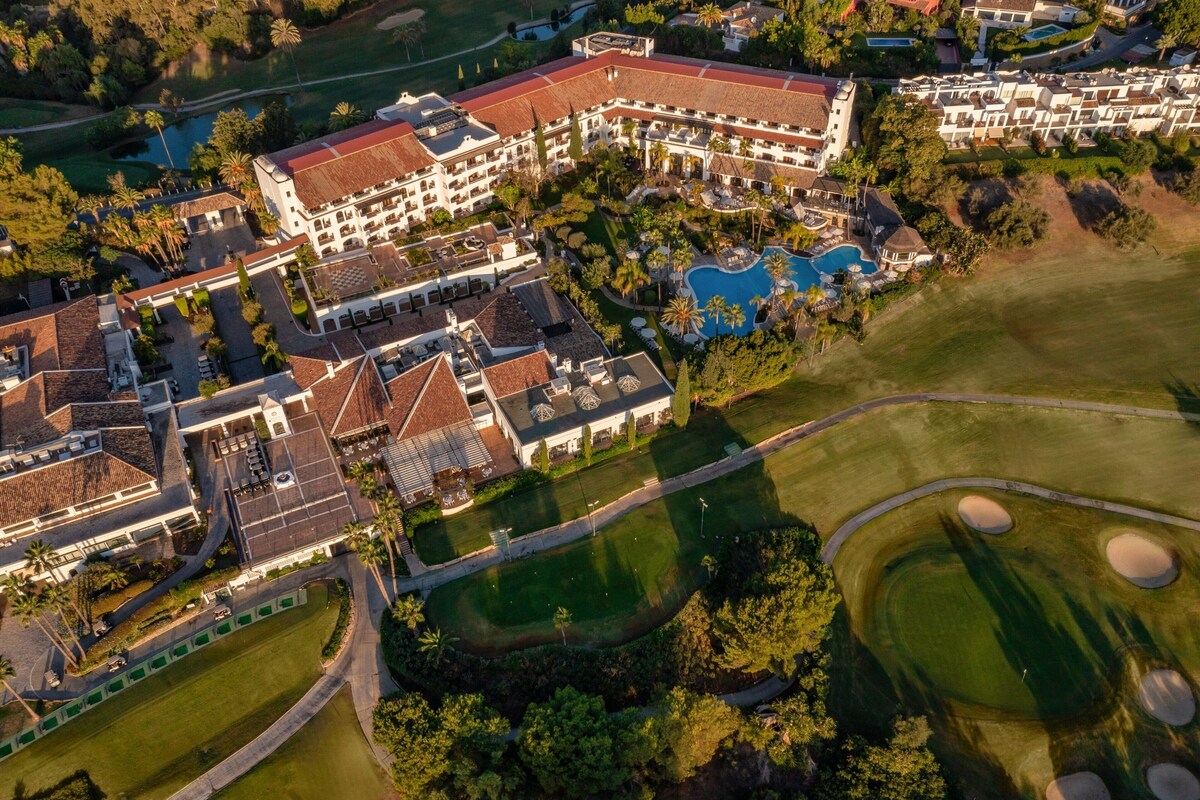Vista aérea de un resort con varias edificaciones, piscina y campo de golf.