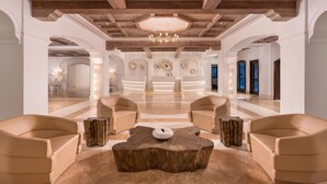 Een ruime lobby met een houten plafond, een centraal zitgedeelte met een ronde tafel, en een receptiebalie op de achtergrond.