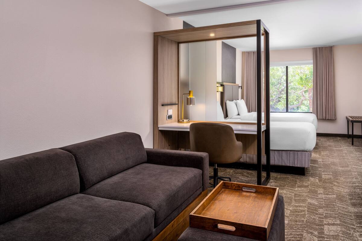 Una habitación de hotel con sofá, escritorio, silla, cama y una ventana grande.