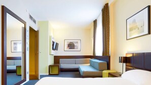 A hotel room with a large bed, a sofa, a TV, and a framed picture on the wall.
