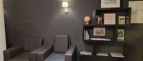 Una habitación con una pared oscura, un sofá, una mesita con un globo terráqueo y una estantería con libros y objetos enmarcados.