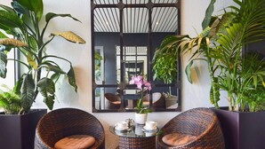 A cozy seating area with wicker chairs and a small table, surrounded by large potted plants.