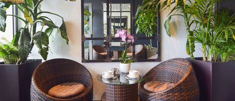 Un coin salon accueillant, avec des fauteuils en osier et une petite table, le tout entouré de grands pots de plantes.