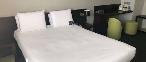 Habitación de hotel con una cama grande, un escritorio, una silla y un taburete pequeño.
