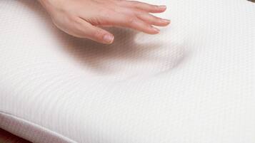 A hand pressing down on a textured white pillow.