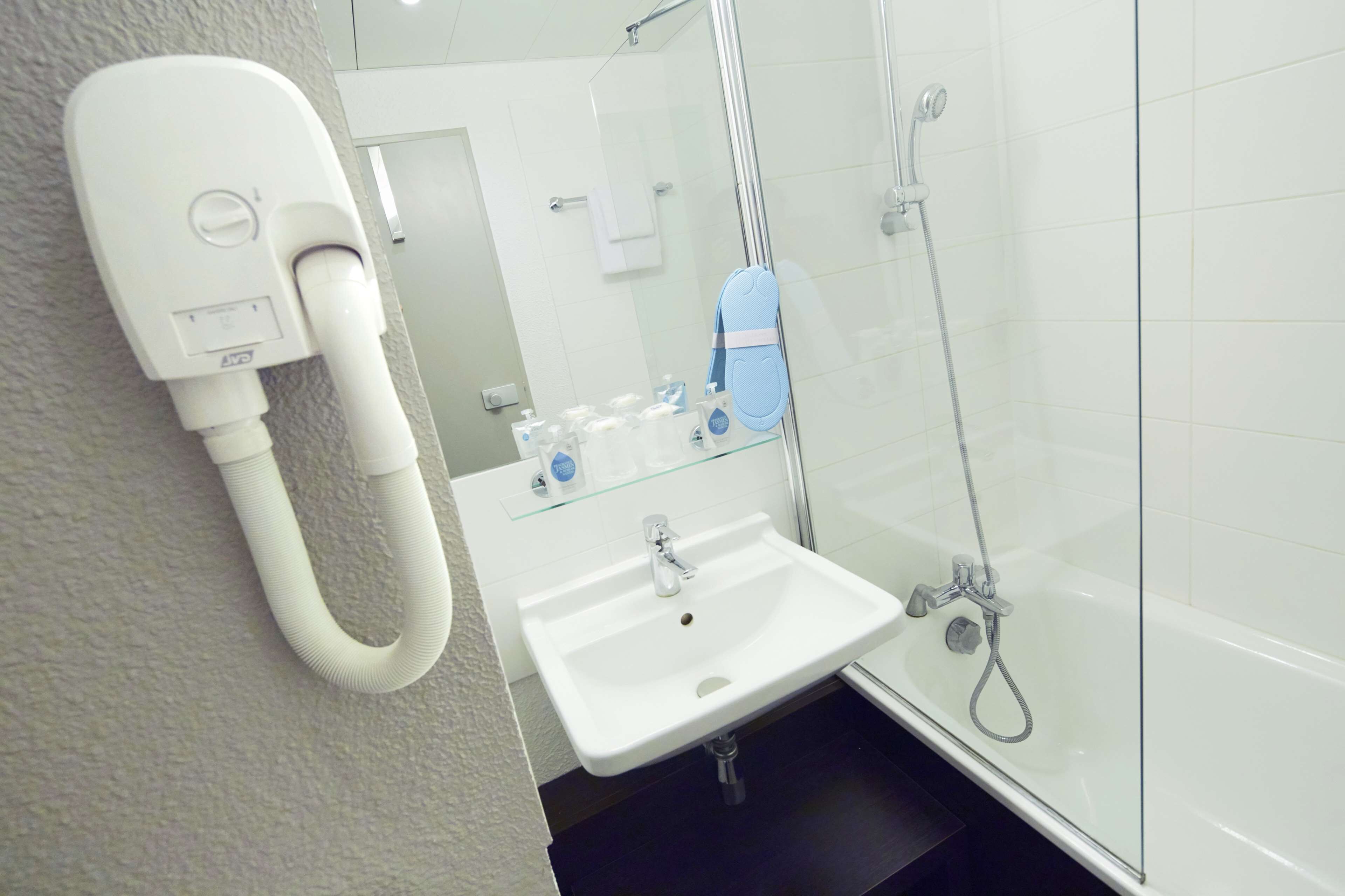 A bathroom with a white sink, glass shower enclosure, and a hand dryer mounted on the wall.